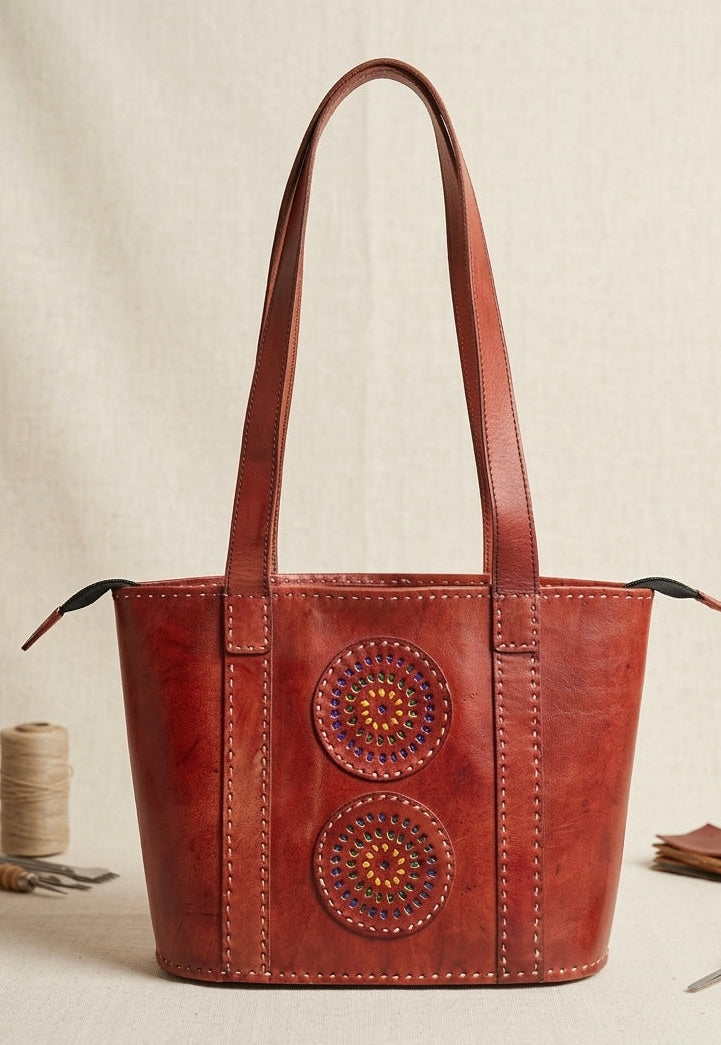 Brown leather tote bag with decorative circular patterns on a beige background