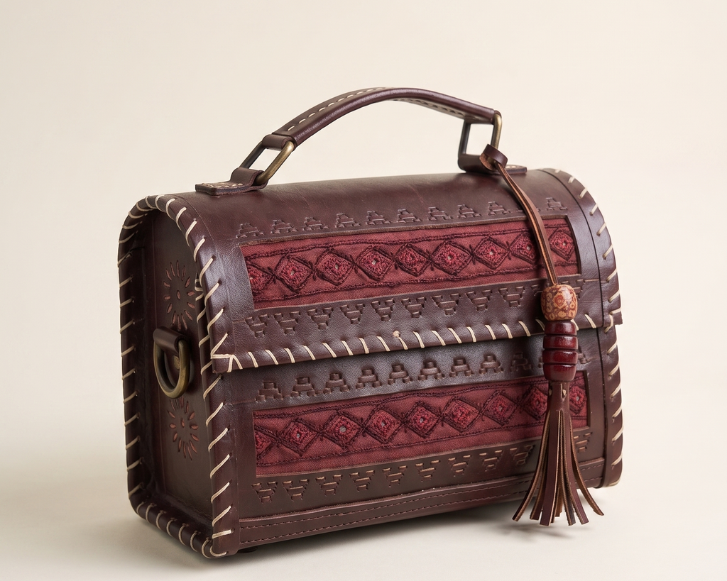 A dark brown leather handbag with embossed geometric patterns, a top handle, and a hanging tassel, photographed on a clean light beige background.