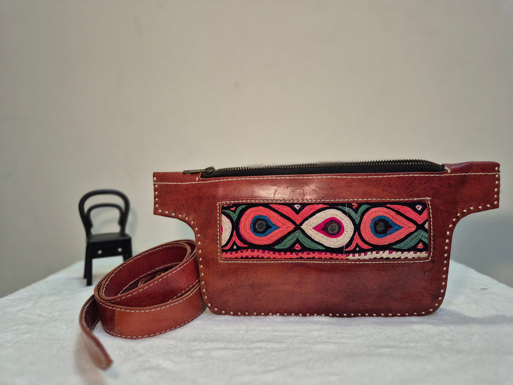 Brown leather waist bag with colorful embroidery on a white surface.