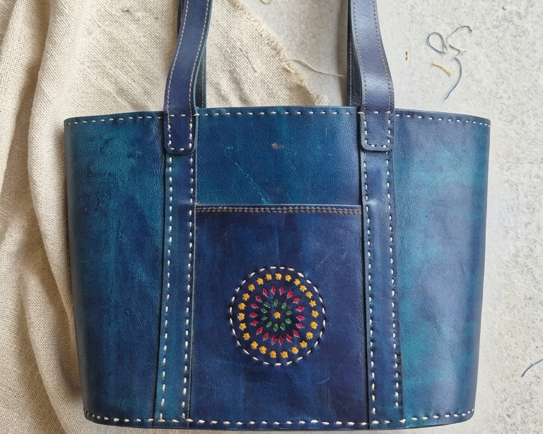Blue leather tote bag with decorative element on a textured surface